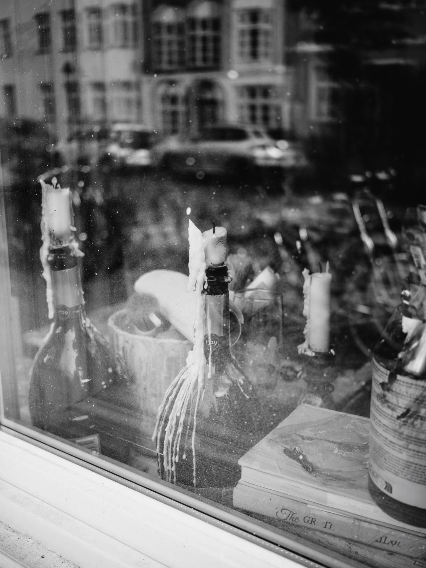 Schwarzweiß-Fotografie eines Schaufensters mit Kerzen und Flaschen, Reflexion einer Straße, Lübecker Altstadt